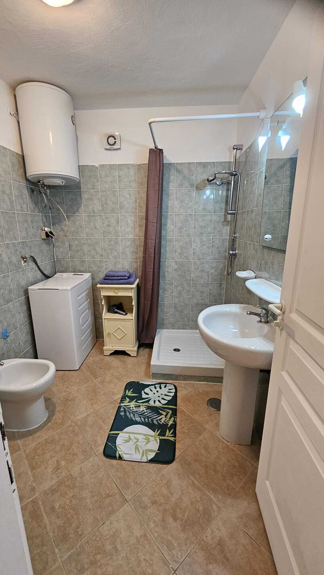 A bathroom with a toilet, bidet, sink, shower, and a towel rack.