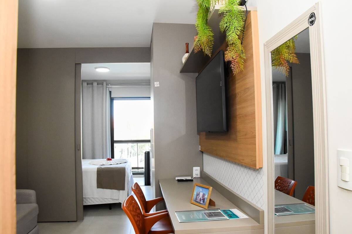 A modern hotel room with a dining area, a TV mounted on the wall, and a view of the balcony.