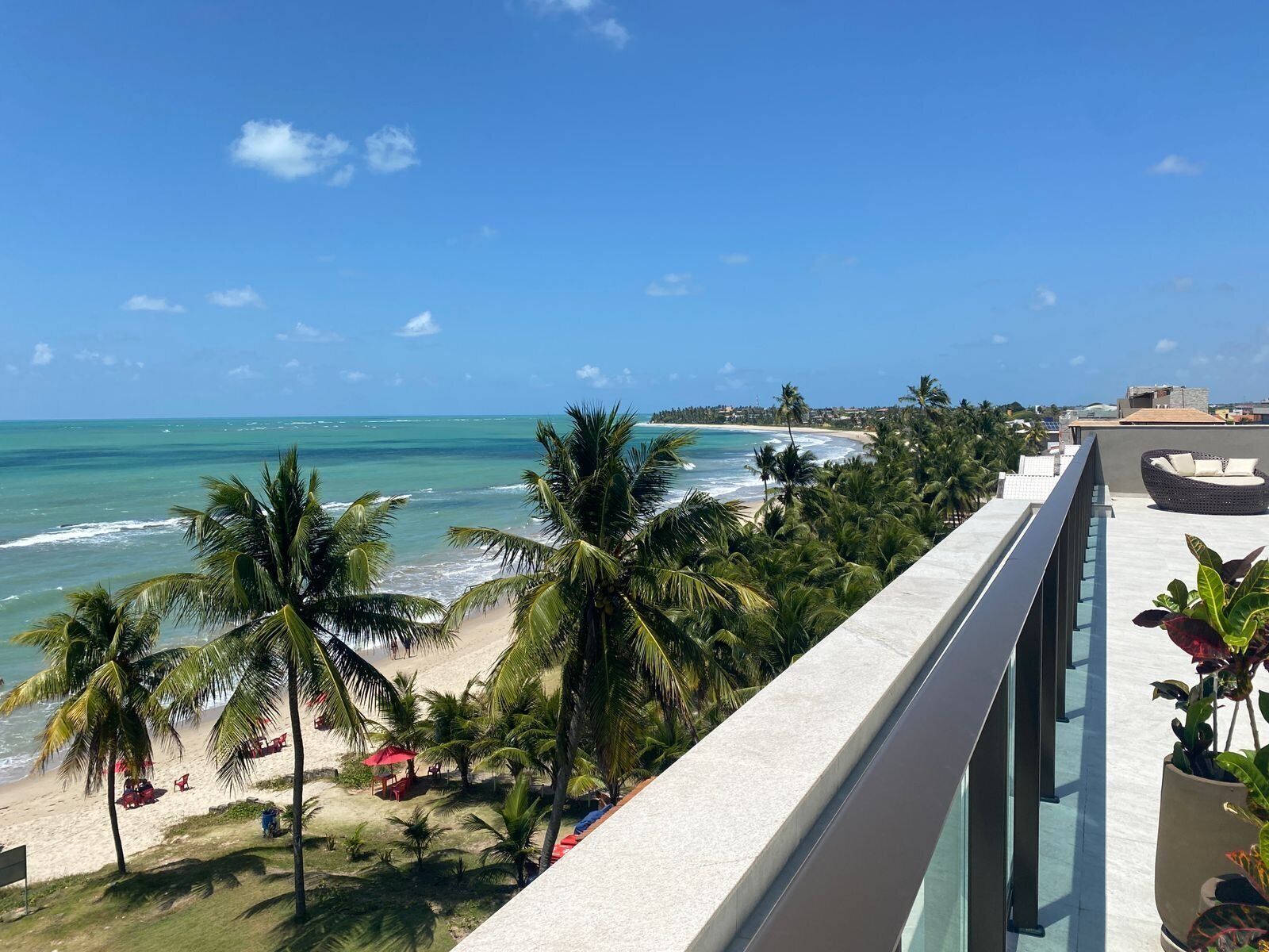 A balcony with a view of a beach, palm trees, and a clear blue sky.