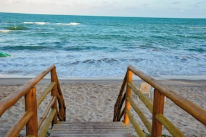 A wooden staircase leading to a sandy beach with the ocean in the background. - Kauai Beach Residence (Tamandaré)