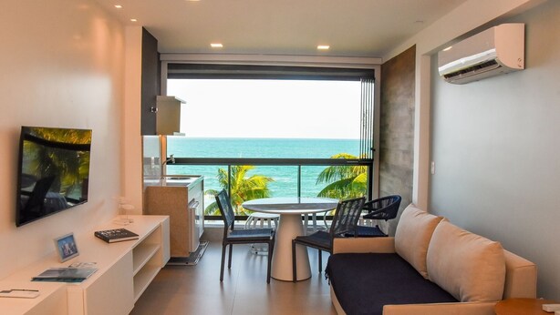 A modern room with a balcony, a sofa, a dining table, and a TV. - Kauai Beach Residence (Tamandaré)