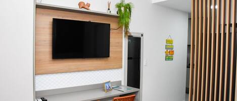 A modern kitchen with a built-in TV, wooden cabinets, two orange chairs, and a refrigerator.
