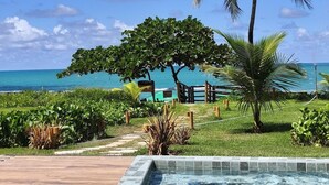 A pool area with a view of the ocean, palm trees, and a wooden deck. - Kauai Beach Residence (Tamandaré)