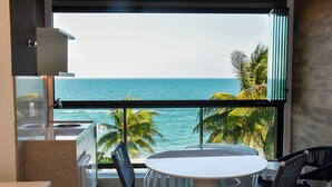 A balcony with a view of the ocean, a round table, and wicker chairs. - Kauai Beach Residence (Tamandaré)