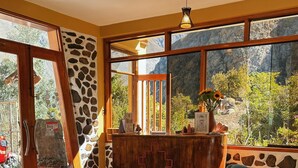 A room with a wooden reception desk, two blue armchairs, a glass coffee table, and large windows with a mountain view. - Sara Garden Lodge (Ollantaytambo)