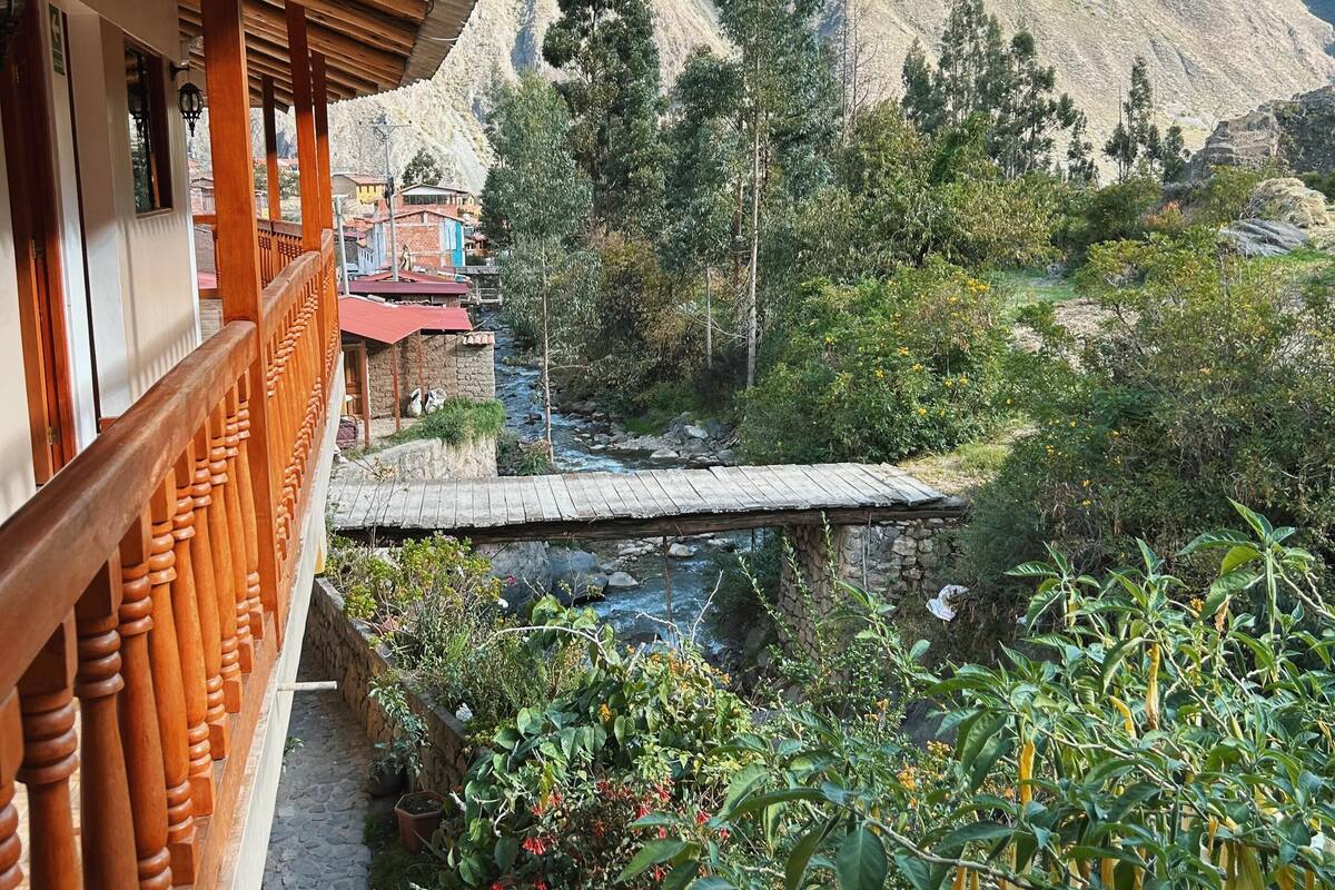 A balcony with wooden railings overlooking a mountainous landscape with a river and greenery.