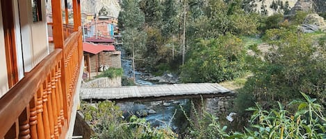 A balcony with wooden railings overlooking a mountainous landscape with a river and greenery.