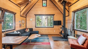 Ein gemütliches Blockhaus-Interieur mit Holzbalkendecke, großen Fenstern, Kamin und einer Couch.