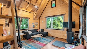 Ein gemütliches Blockhaus-Interieur mit Holzbalkendecke, großen Fenstern, einem Kamin und einer Couch.