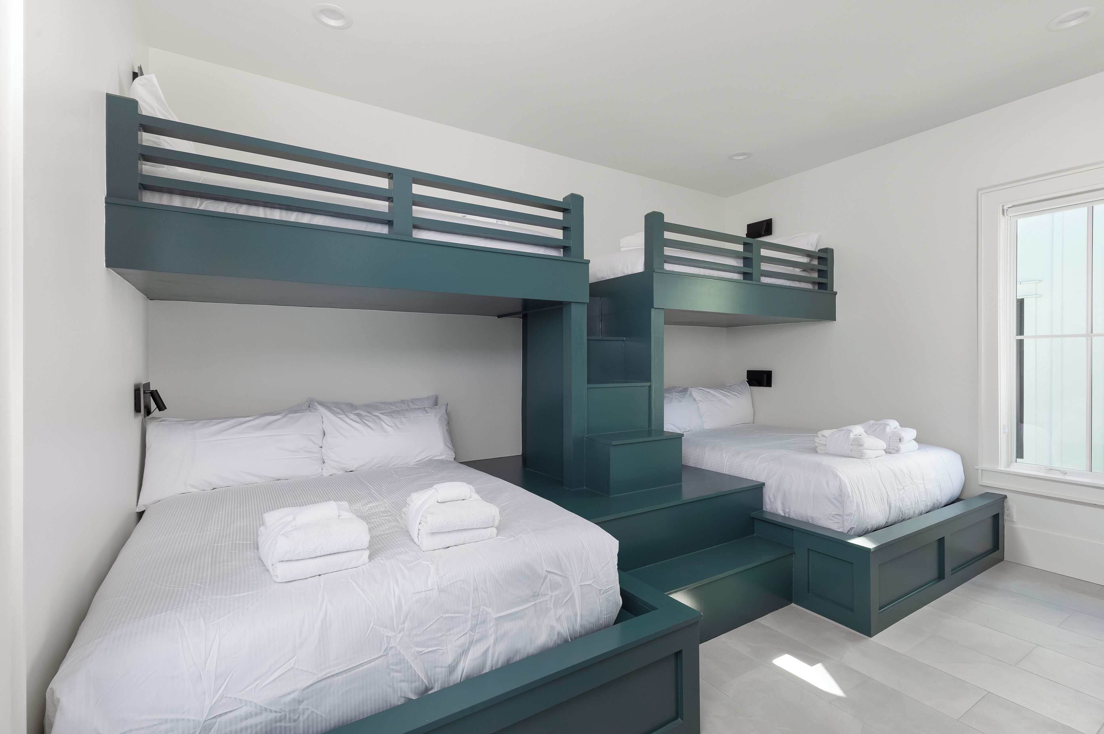 A room with bunk beds, white bedding, and a window.