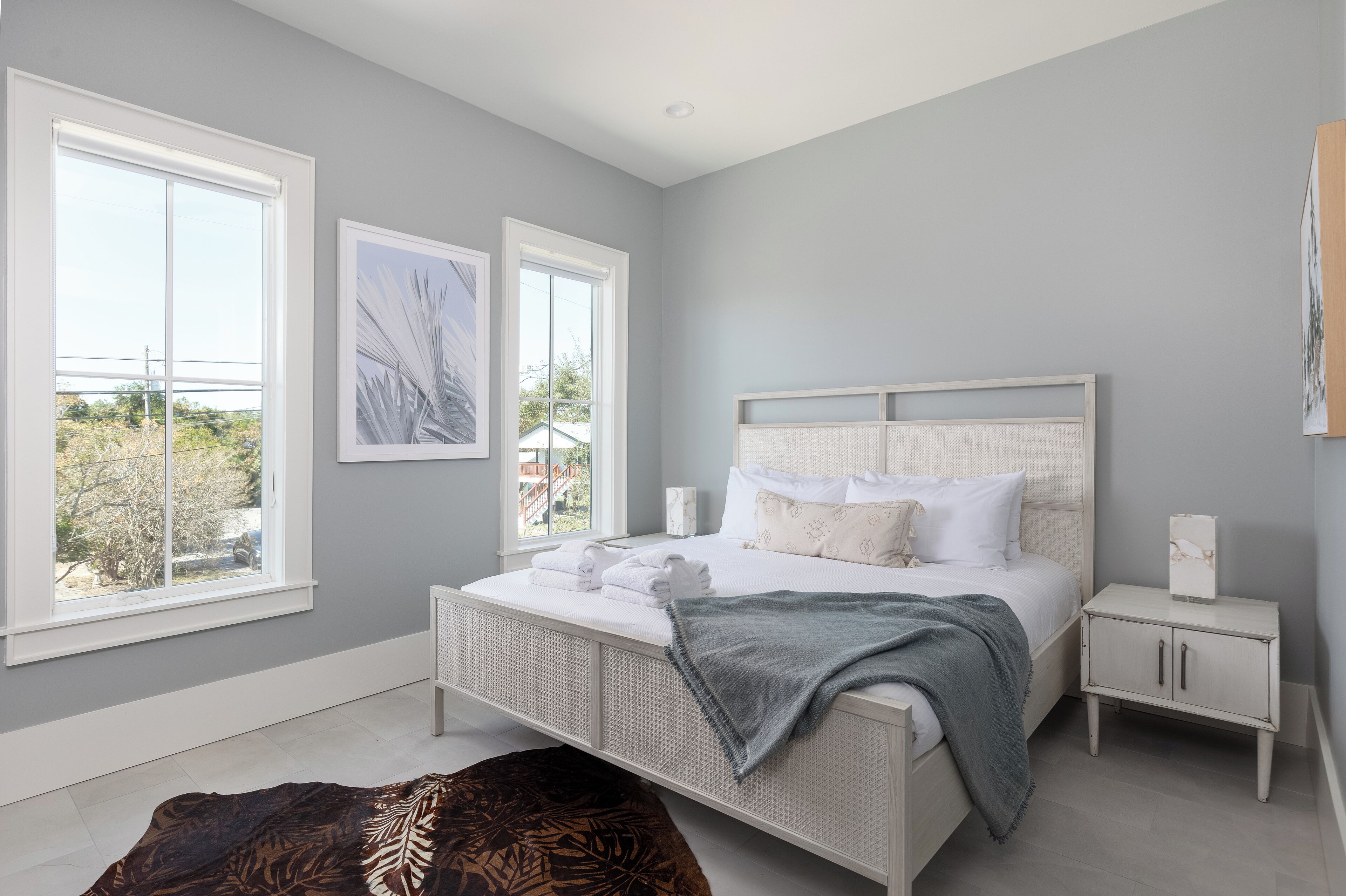 A bedroom with a large bed, two windows, a bedside table, and a nightstand.