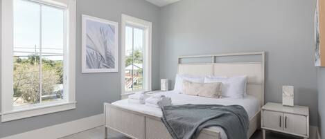 A bedroom with a large bed, two windows, a bedside table, and a nightstand.