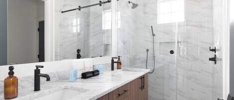 A modern bathroom with a large mirror, marble countertop, and a glass-enclosed shower area.