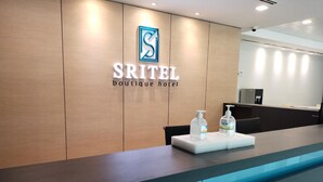 A reception desk with a logo and name 'Sritel Boutique Hotel' on the wall. There are two hand sanitizer bottles on the counter. - Sritel Boutique Hotel (Shah Alam)