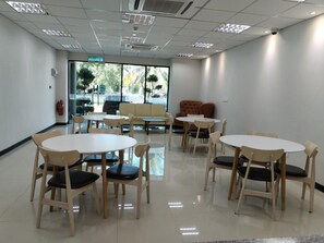 A conference room with round tables and chairs, a sofa, and a large window with a view of trees and a street. - Sritel Boutique Hotel (Shah Alam)