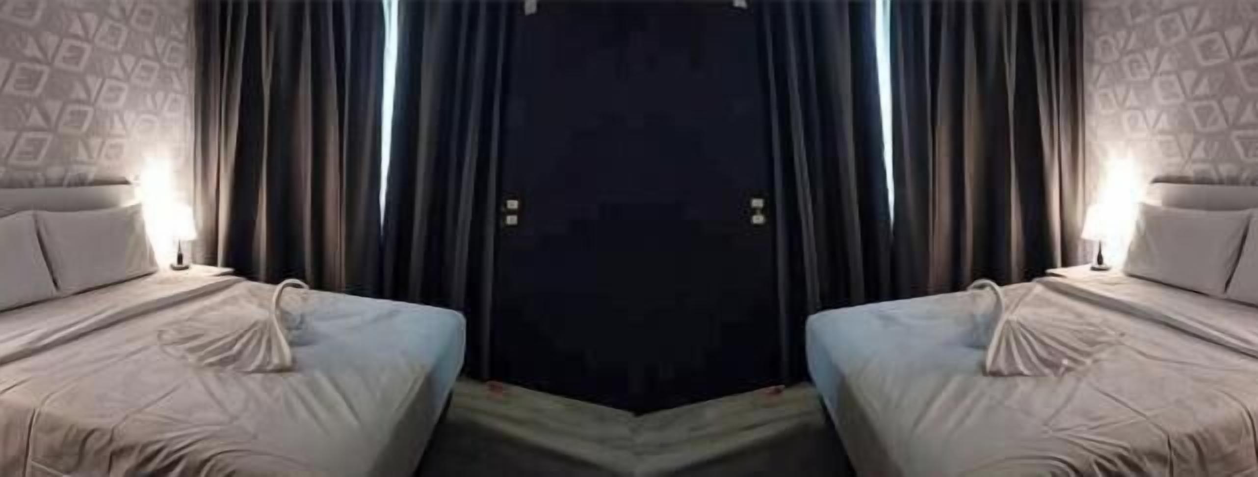 A hotel room with two beds, a dark door, and a patterned wall.