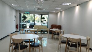 A conference room with round tables and chairs, a sofa, and a large window with a view of trees and a street. - Sritel Boutique Hotel (Shah Alam)