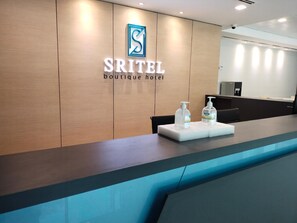 A reception desk with a logo and name 'Sritel Boutique Hotel' on the wall. There are two hand sanitizer bottles on the counter. - Sritel Boutique Hotel (Shah Alam)