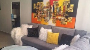 A modern living room with a grey sofa, a round coffee table, and a colorful abstract painting on the wall.