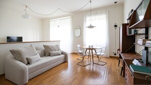 Ein modernes Wohnzimmer mit einer Couch, einem Esstisch mit Stühlen, einem Bücherregal und einem Fernseher an der Wand.