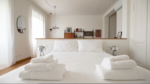 Ein modernes Schlafzimmer mit einem großen Bett, zwei Nachttischen mit Lampen, einem Holz-Kopfteil, einem Spiegel und einem Regal mit Büchern und Bildern.