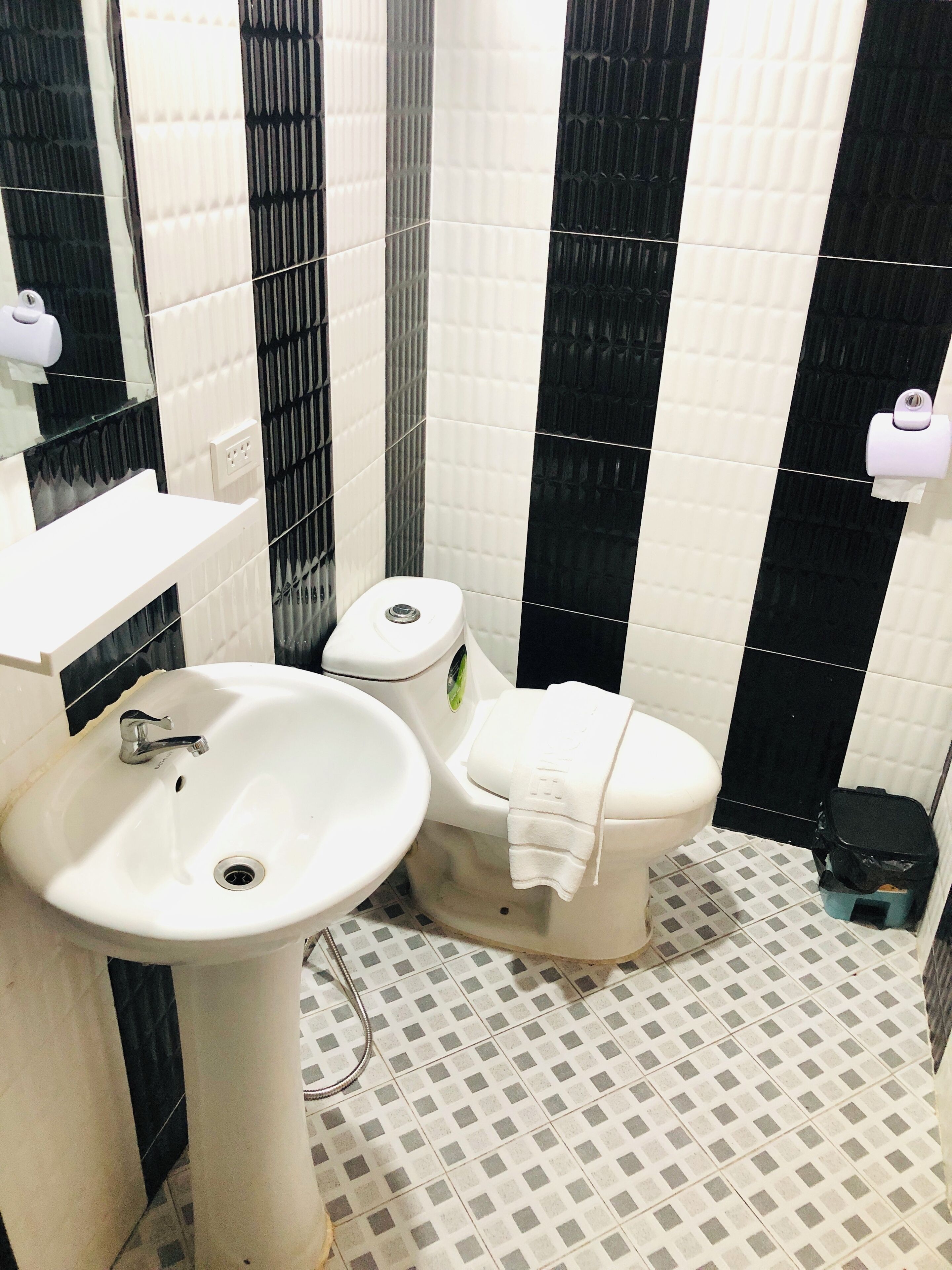 A bathroom with a white sink, a toilet, and black and white tiled walls.