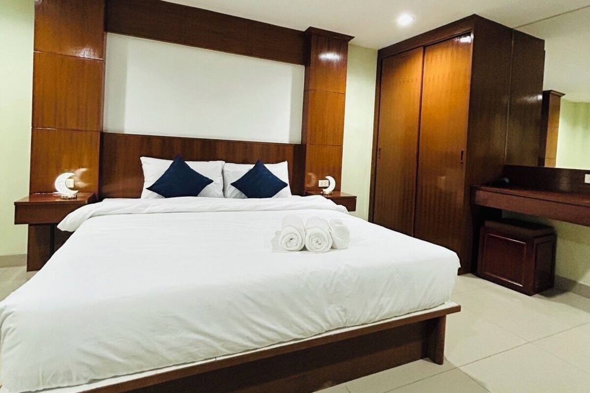 A hotel room with a large bed, wooden headboard, and a ceiling fan.