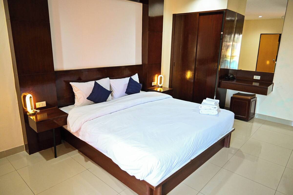 A hotel room with a large bed, wooden headboard, two bedside tables with lamps, a wardrobe, and a mirror.