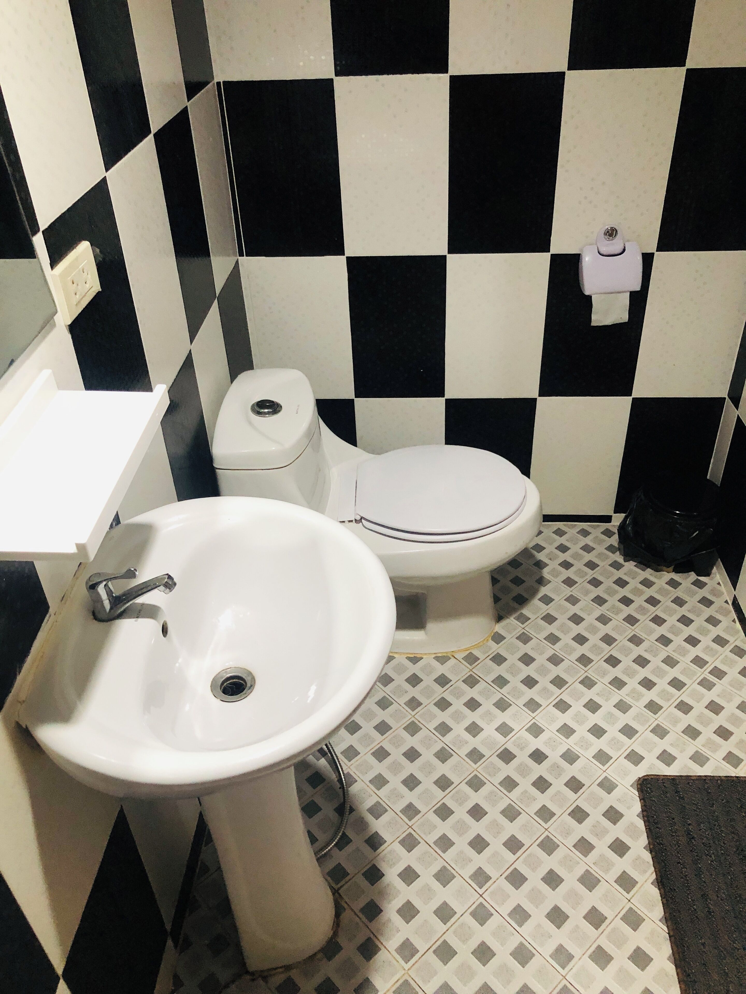 Un baño con lavamanos blanco, inodoro y un bote de basura negro.