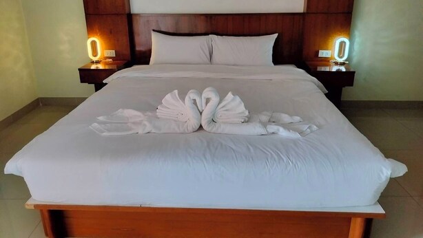 Ein Hotelzimmer mit einem großen Bett, zwei Nachttischen mit beleuchteten Ziffern und einem ordentlich bezogenen Bett mit Handtüchern, die zu einem Schwan geformt sind.