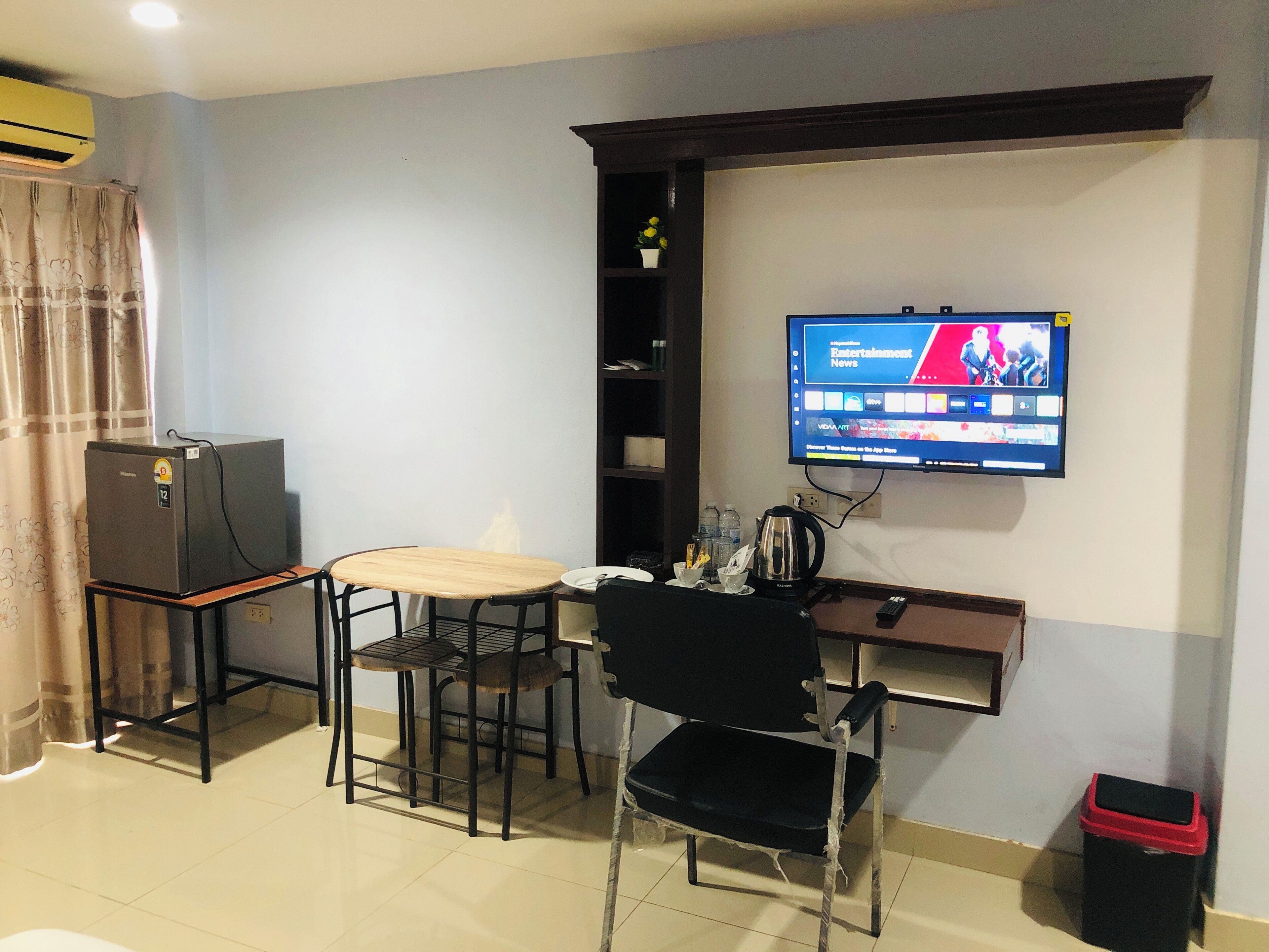 Un espace de vie compact comprenant un téléviseur fixé au mur, une petite table, deux chaises, un mini-réfrigérateur et une poubelle.