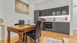 A modern kitchen with a marble backsplash, a dining area with a wooden table and chairs, and a herringbone-patterned floor.