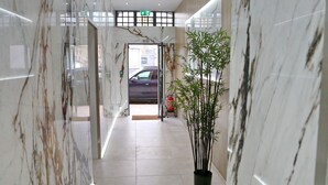 A marble hallway with a potted plant, a fire extinguisher, and a car visible through the door.