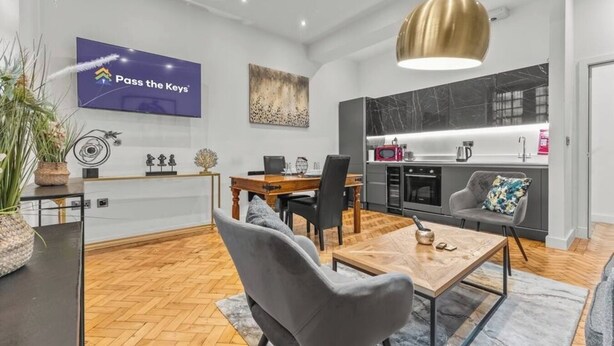 A modern kitchen with a marble backsplash, a dining area with a wooden table and chairs, and a living area with a sofa and a coffee table.