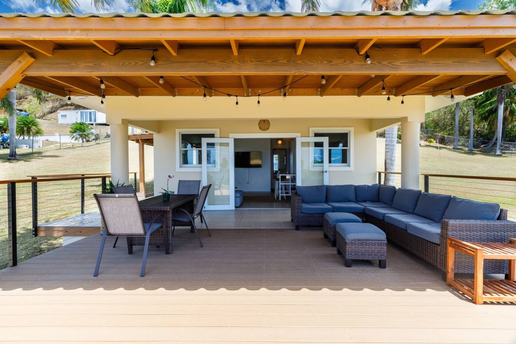A covered outdoor patio with a dining table and chairs, a sofa, and a small table with a plant.