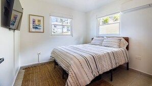 Une chambre à coucher avec un lit, deux fenêtres, un téléviseur et une affiche encadrée au mur.