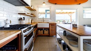 Une cuisine moderne avec des carreaux de céramique blancs disposés en motif métro, des plans de travail en bois, une cuisinière à gaz et une planche de surf accrochée au mur.