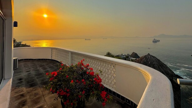 A balcony with a view of the sea and ships, a potted plant with red flowers, and a white railing. - Casa Vita La Punta (Manzanillo-Colima)