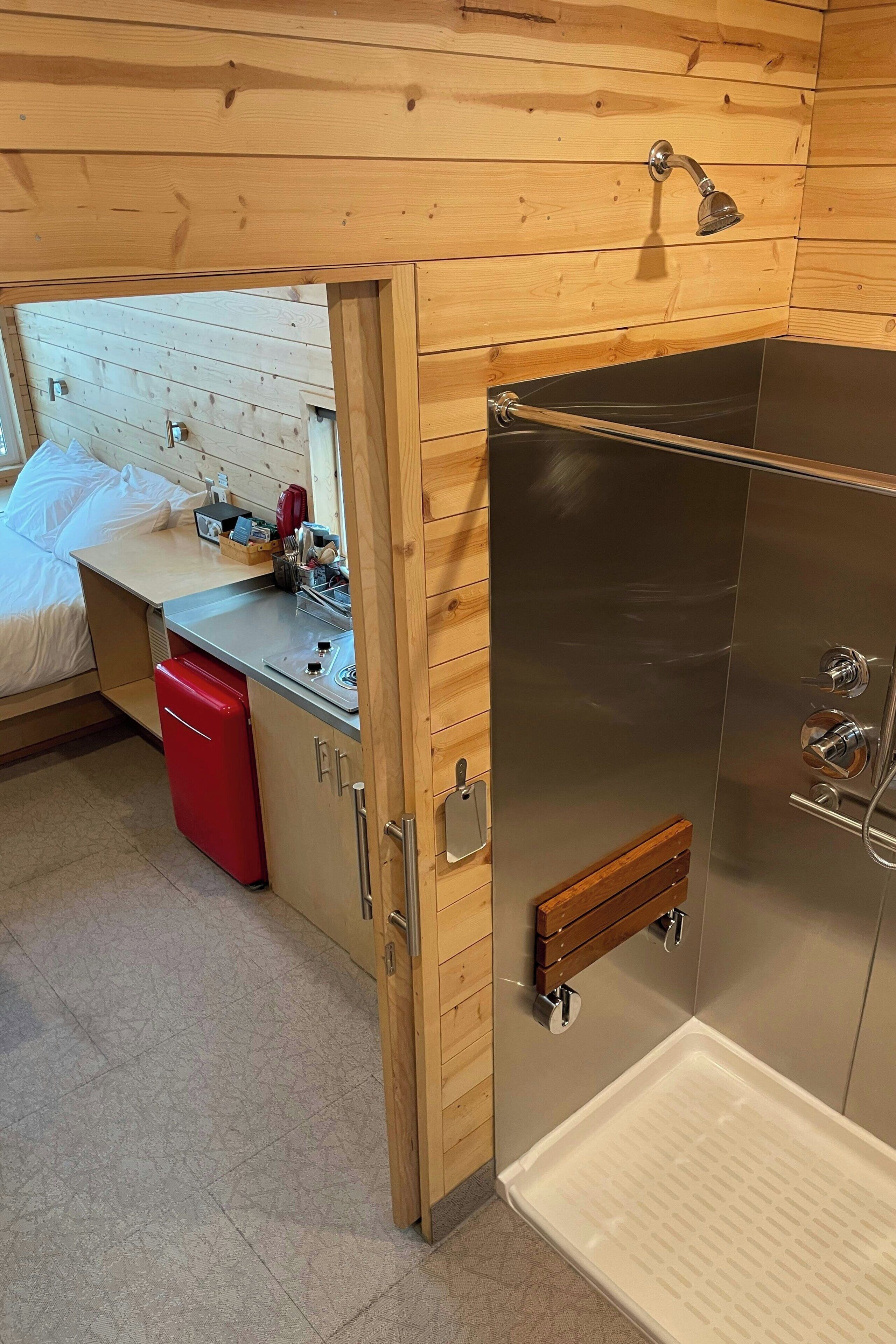 A compact room with a bed, a small kitchenette, and a shower area.