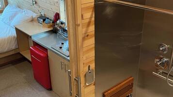 A compact room with a bed, a small kitchenette, and a shower area.