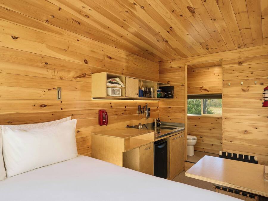 A wooden cabin interior with a bed, kitchenette, and a small bathroom.