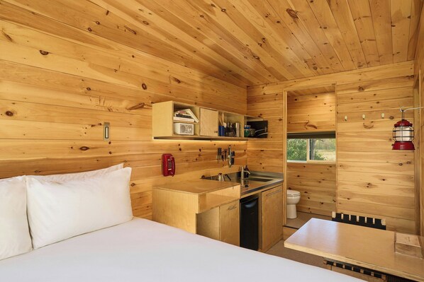 A wooden cabin interior with a bed, kitchenette, and a small bathroom.