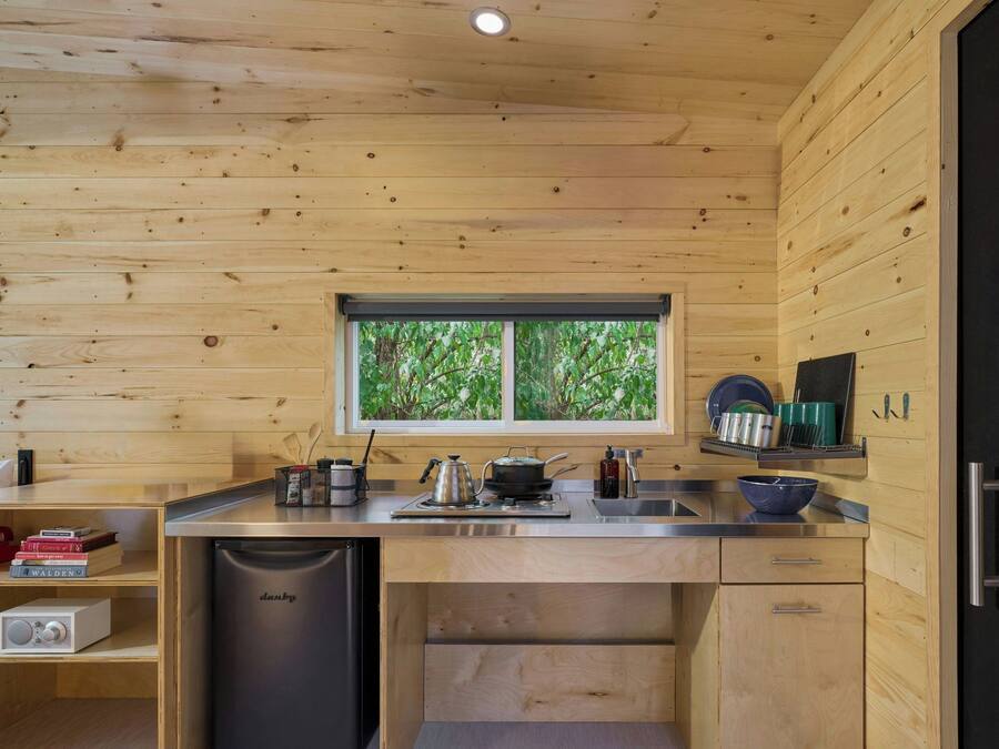 A compact kitchen with wooden walls, a window with a view of greenery, a built-in dishwasher, and a sink.