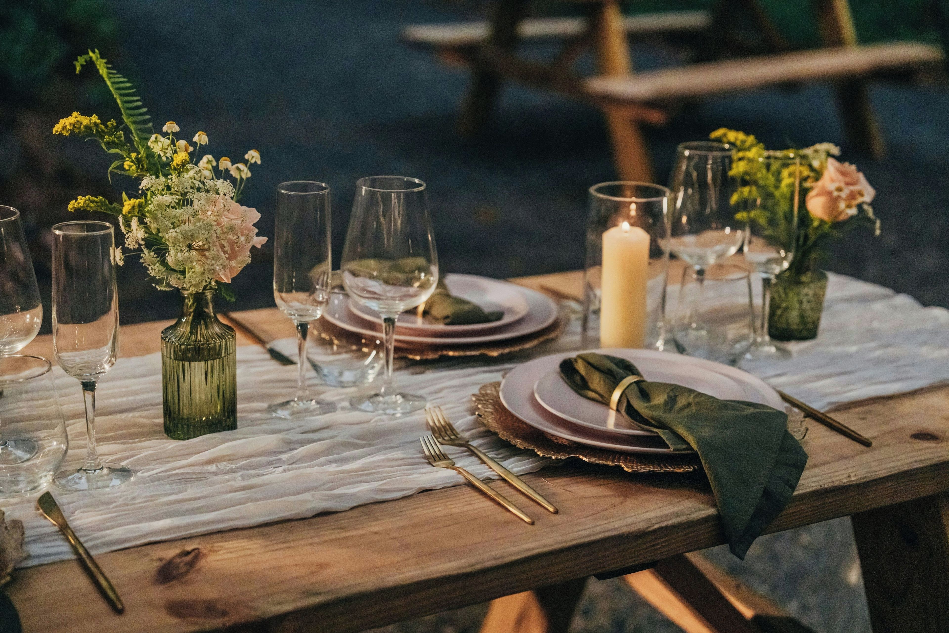 A wooden table set for a meal with glassware, plates, and cutlery.