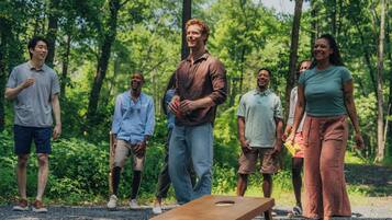 A group of people standing in a forested area with a wooden board game in the foreground.