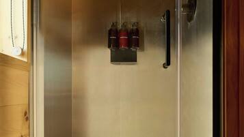 A shower enclosure with a glass door, a white shower base, and a control panel with bottles.