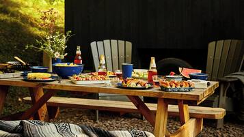 Une cabane en bois rustique, avec une table à manger dressée pour un repas, entourée de forêt.