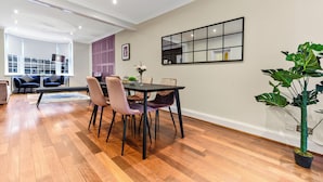 A modern dining area with a wooden floor, a dining table with chairs, a large mirror, and a potted plant. - Luxurious Pad in an Unbeatable Wembley Location (Wembley)