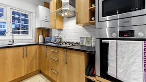 A modern kitchen with wooden cabinets, stainless steel appliances, and a window. - Luxurious Pad in an Unbeatable Wembley Location (Wembley)