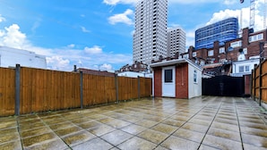 A courtyard with a tiled floor, a wooden fence, and a small building with a door. - Luxurious Pad in an Unbeatable Wembley Location (Wembley)